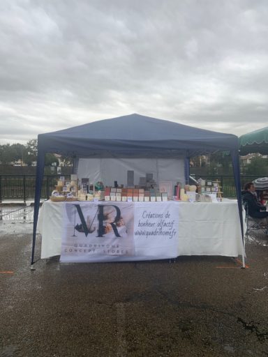 Stand de marché avec un auvent bleu et divers produits exposés sur une table.